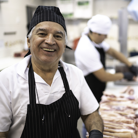 Smiling man in a cap and apron in a butcher shop